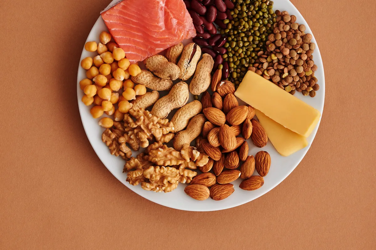 A plate of high-protein foods: salmon, kidney beans, lentils, chickpeas, nuts and cheese