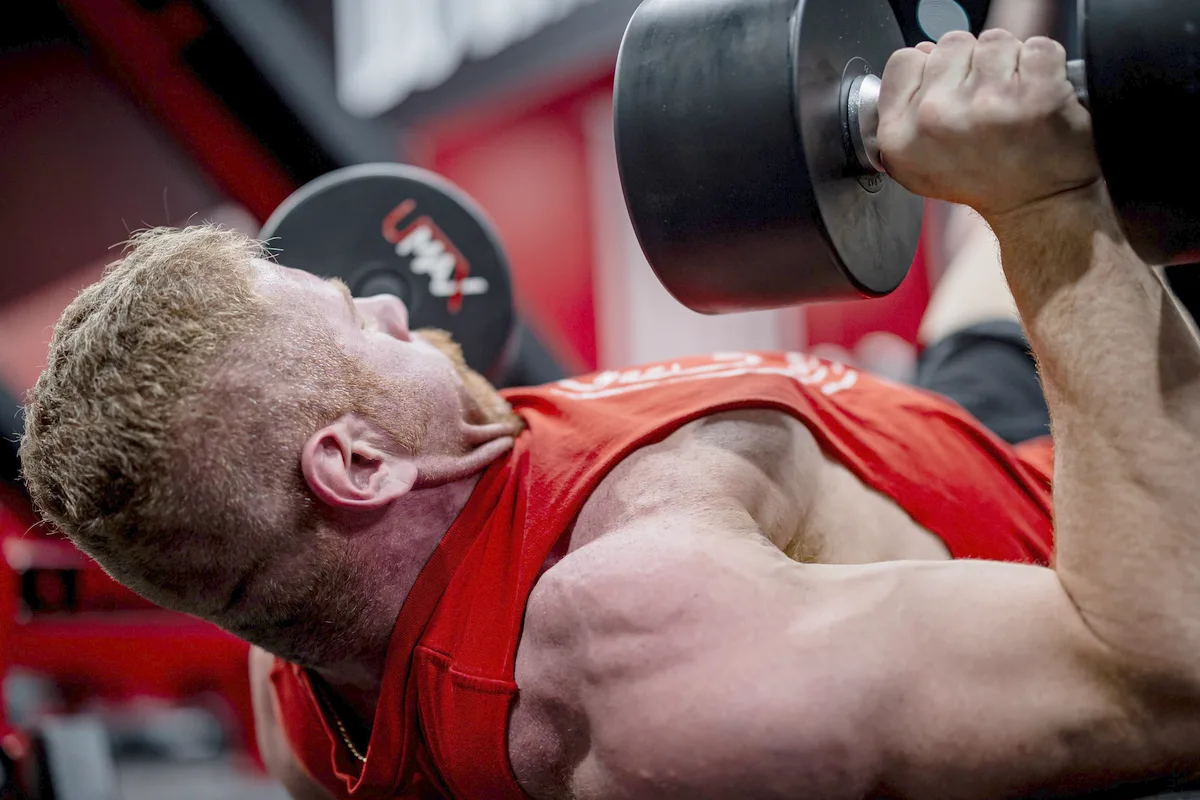 A lifter pressing a heavy dumbbell during a demanding set