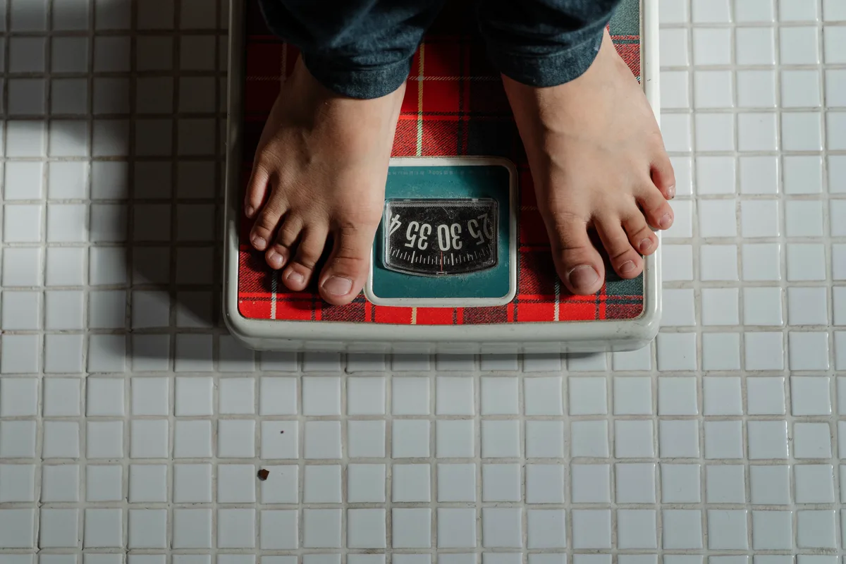 Bare feet standing on a weighing scale on a tiled bathroom floor