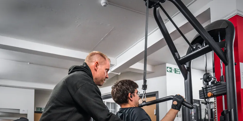 Trainer guiding a member's form during a cable machine exercise